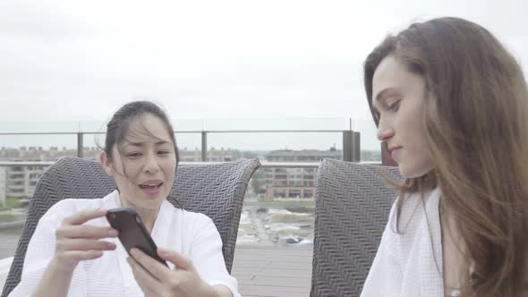Women laughing at smartphone while relaxing at spa
