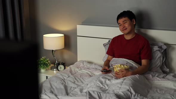 happy young man watching TV on a bed at night