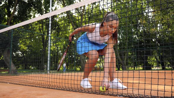 woman bending down to pick a tennis ball