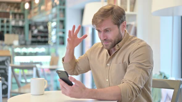 Disappointed Man Reacting To Loss on Cellphone in Cafe alt