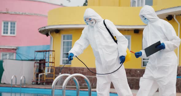 Two doctors team in protective suits disinfect swimming pool, control sanitation	 alt