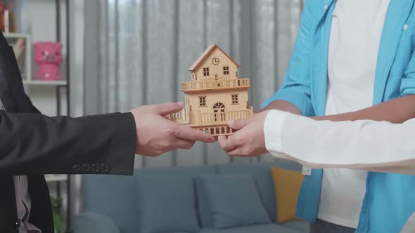 Close Up Of Couple'S Hands Receiving The House Model From A Real Estate Agent In The House For Sale alt