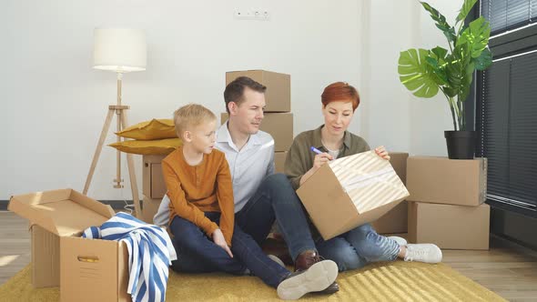 Happy Family Moving to New Place Sitting Holding Marker Pen Writing Carboard Boxes
