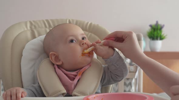 A newborn baby with a spoon tries to eat on its own. Feeding a newborn with pumpkin puree alt