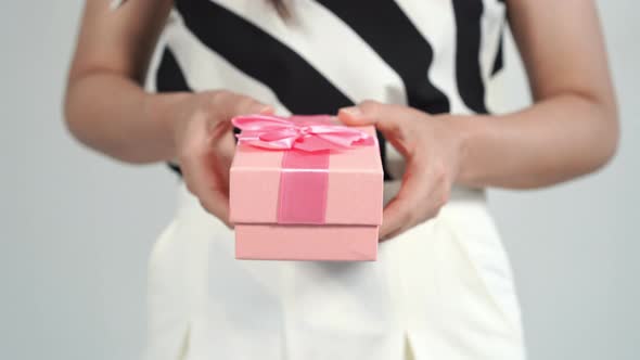 woman holding a pink gift box in a gesture of giving.