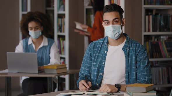 Students in Library Young Indian Guy in Protective Mask Sits at Desk Doing Homework Preparing for alt
