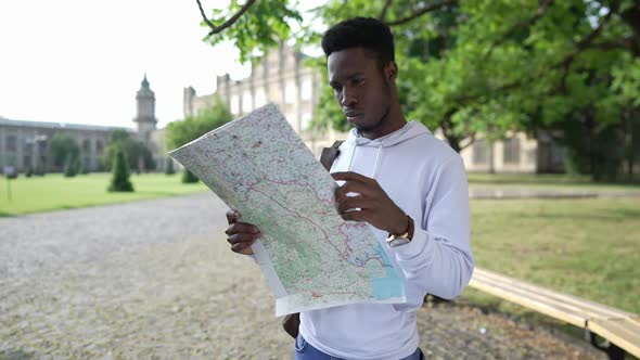 Portrait of Concentrated African American Young Man with Paper Map Standing at University Campus alt