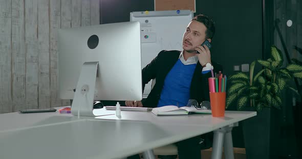 Businessman in the Office in Front of the Computer Talking on the Phone alt