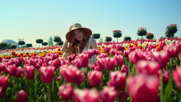 Camera Tracking Aroung Pretty Girl in Sunhat Sitting in Pose in Red Tulip Field alt