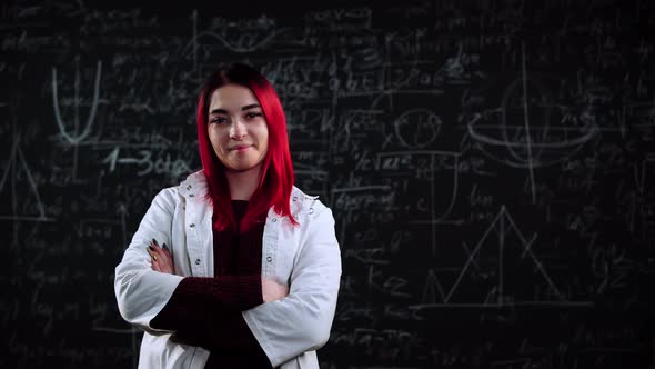 A Woman with Red Hair in Lab Coat Stands in Front of Chalkboard Full of Algebra Formulas alt