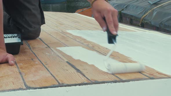 Applying thinned coat white primer on wooden boat roof with roller alt