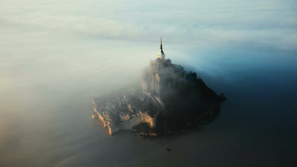 Epic Aerial Shot of Ethereal Mont Saint Michel Island Castle Covered with Amazing Sunrise Fog Clouds alt