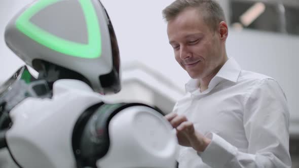 A Man Stands with a Robot Bot and Asks Him Questions and Asks for Help By Clicking on the Screen on alt