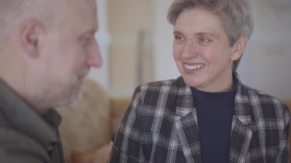 Adult Man Treats His Mature Wife with a Chocolate Bar While Sitting on a Sofa in a Room alt