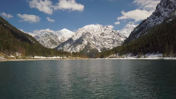 Low angle aerial view above Plansee lake Austria towards cold mountain snow covered summit landscape alt