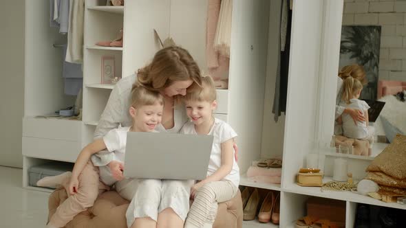 Mom with Twin Daughters at the Laptop on the Background of the Closet