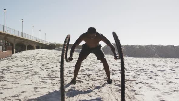 African american man exercising with battling ropes outdoors on the beach alt