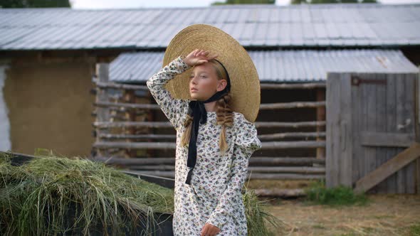 Beautiful Girl with Two Braids in Hat and Romantic Dress Looking Away on Rural Landscape in alt