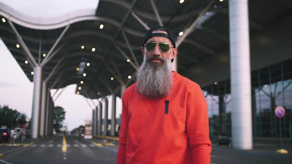 Portrait of Handsome Stylish Mature Man with Long Gray Beard Wearing Cap and Sunglasses on Urban alt