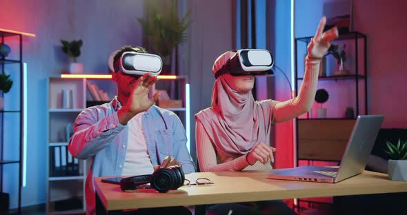 Man and Arabic Woman in Hijab Working on Imaginary Screen in Augmented Reality Goggles in home alt