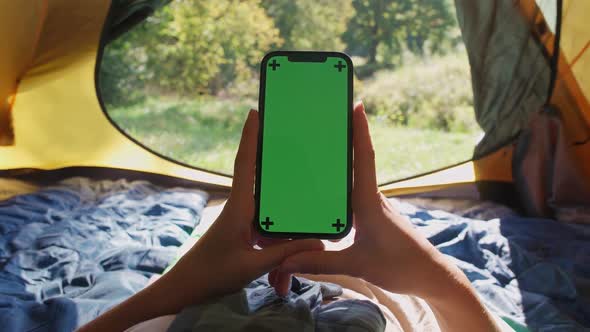 Handheld Firstperson View Woman Holding a Smartphone with a Green Screen While Lying in a Tent alt