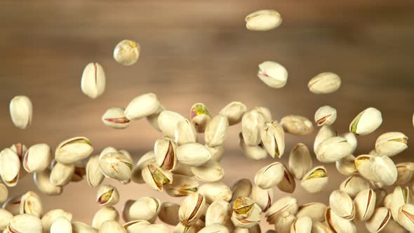 Super Slow Motion Shot of Flying Pistachios After Being Exploded on Wooden Background at 1000Fps alt