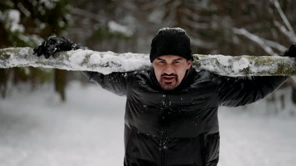 Powerlifter is Training in Nature Carrying Log in Winter Forest Holding Weight on Shoulders alt