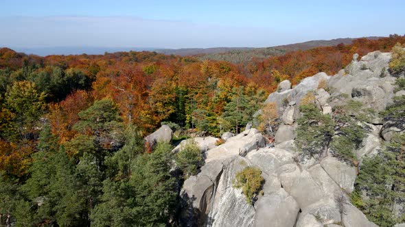 Aerial Orbit View of Couple Hikers on the Top of the Rock in the Middle of the Autumn Forest alt