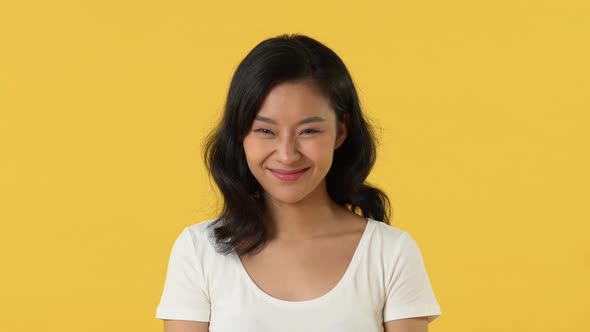 Pretty young Asian girl in white plain t-shirt smiling on yellow studio background