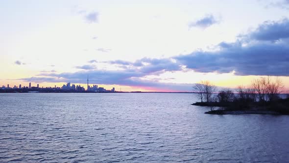 Aerial flying over the water with a view of the beautiful Toronto skyline at sunrise. alt
