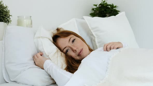 beautiful sleeping female wakes up in bed in  morning and opens her eyes