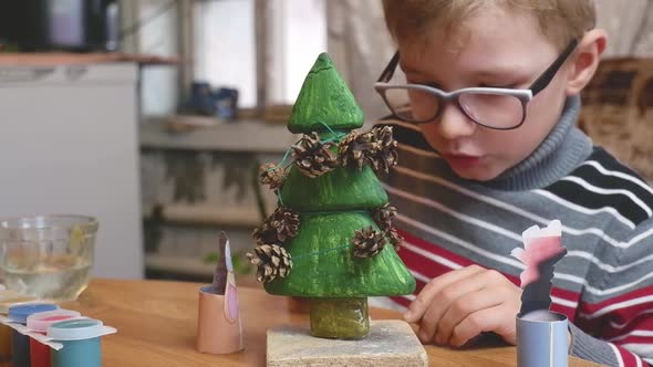 A Little Boy Decorates a Handmade Christmas Tree with Pine Cones and at the Same Time Plays Funny