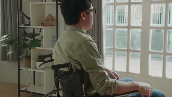 Asian Man Sitting In A Wheelchair Looking Out Of A Door alt