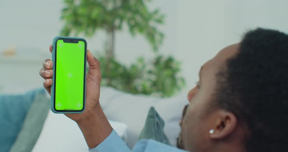 Man Lying on Couch with Modern Smartphone in His Hand While Looking on Mock Up Screen with Trecking