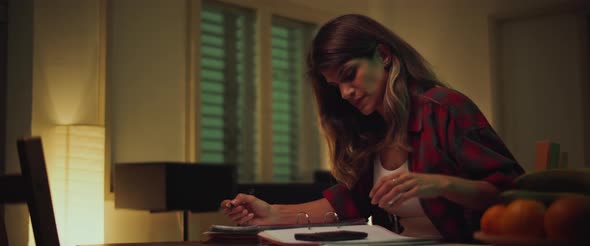 Young woman sitting at desk, studying at home in the evening, making notes  alt