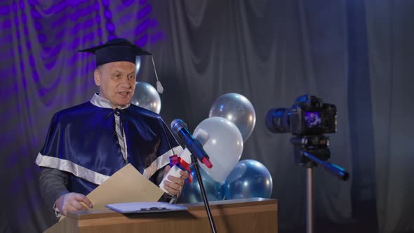 Male Lecturer in Mantle Congratulates Online University Graduates Standing at Chair in Conference alt