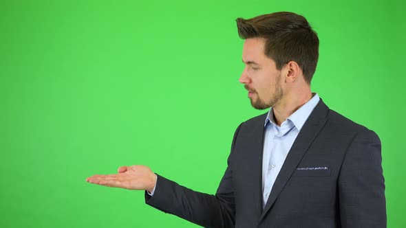 A Young Businessman Talks To the Camera, Puts Out a Hand with a Product and Continues Talking alt