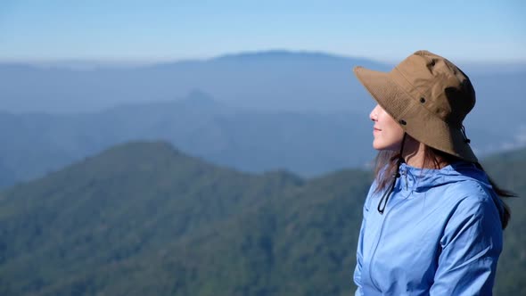 Slow motion of a female traveler standing on mountain peak, looking at a beautiful view