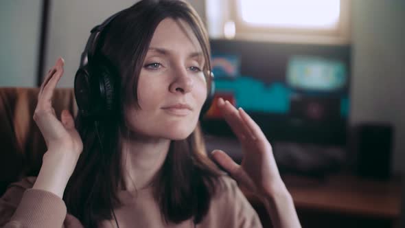 A beautiful girl in big headphones listens to music in a chair at the computer, dancing. equalizer