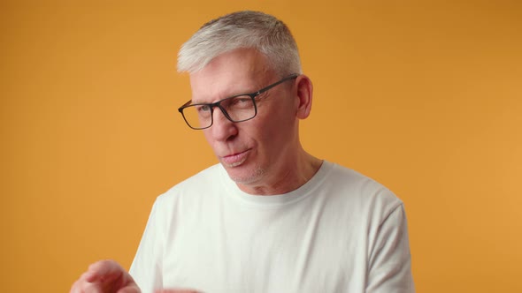 Senior Man in Glasses Talking to Someone Against Yellow Background in Studio