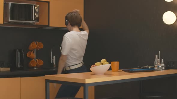 Young Cheerful Woman in Headphones Dancing in Kitchen and Leaving with Apple. Portrait of Joyful alt