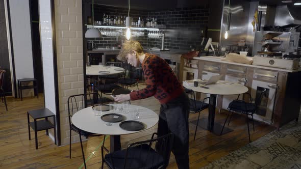 Slomo of Young Woman Moving Plates From Round Restaurant Table alt