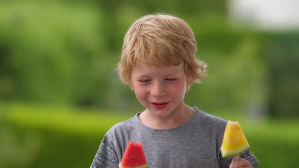 Young Blond Boy Eating Red and Yellow Watermelon on Stick