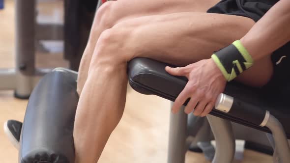 Closeup View of the Man Athlete with Muscular Legs Working Out at the Gym Leg Curl Trainer alt
