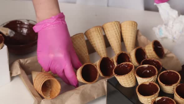 Wafer Cones Smeared With Liquid Chocolate. The Woman Puts Them On The Rack alt