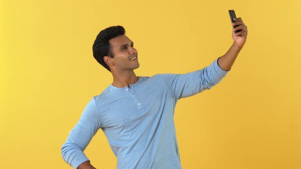 Casual smiling young Indian man taking selfie on his smartphone