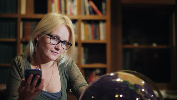 Woman with a Smartphonee in Hand Looks at the Globe alt