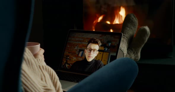 Woman Makes Online Video Call on Laptop in Cozy Home with Fireplace