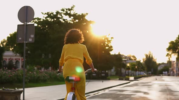 Back View of an Unrecognizable Woman in Long Yellow Dress Riding a City Bicycle in the City Center alt