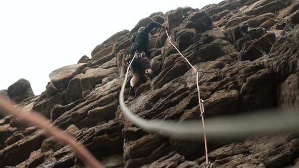 A Male Climber Insures a Rope Climbing a Rocky Route in the Rain alt